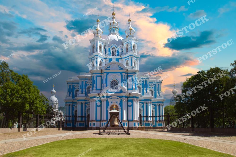 На фотографии изображен Смольный собор — один из самых красивых примеров елизаветинского барокко в Санкт-Петербурге, построенный по проекту архитектора Бартоломео Растрелли. Собор выделяется своим голубым фасадом с белыми декоративными элементами и золотыми куполами. Это знаковое место, расположенное в Смольном монастыре, давно стало символом архитектурной роскоши Петербурга.